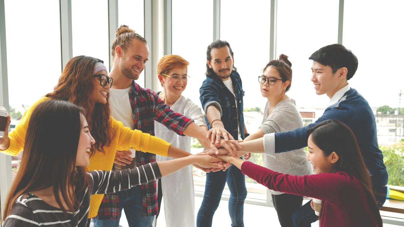 Diverse team smiling and joining hands in a group huddle in a bright office.