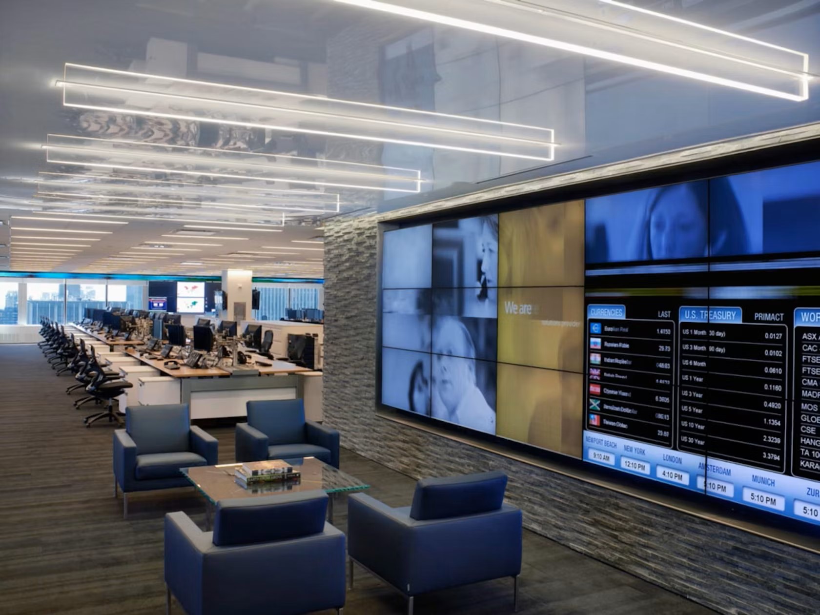 Modern office with rows of desks and computer monitors, a digital wall display.