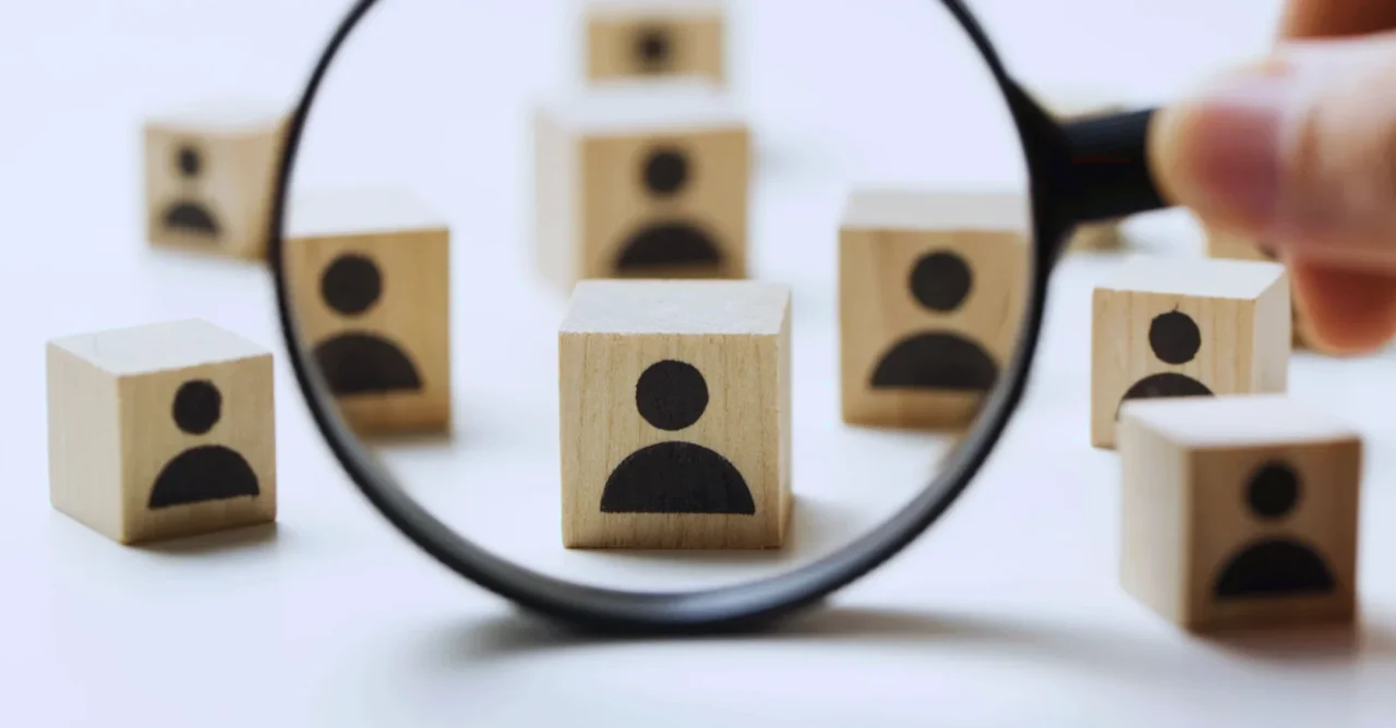 Magnifying glass focusing on one person icon among a group of wooden blocks.