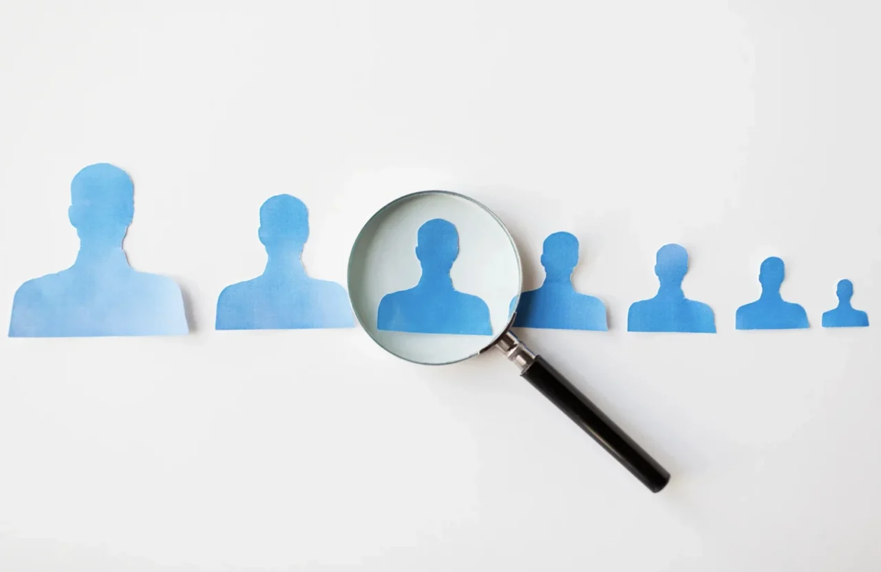 Magnifying glass highlighting one candidate among a row of blue silhouettes.